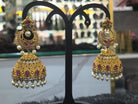 Ornate gold earrings with pearls and gemstones on a black stand.
