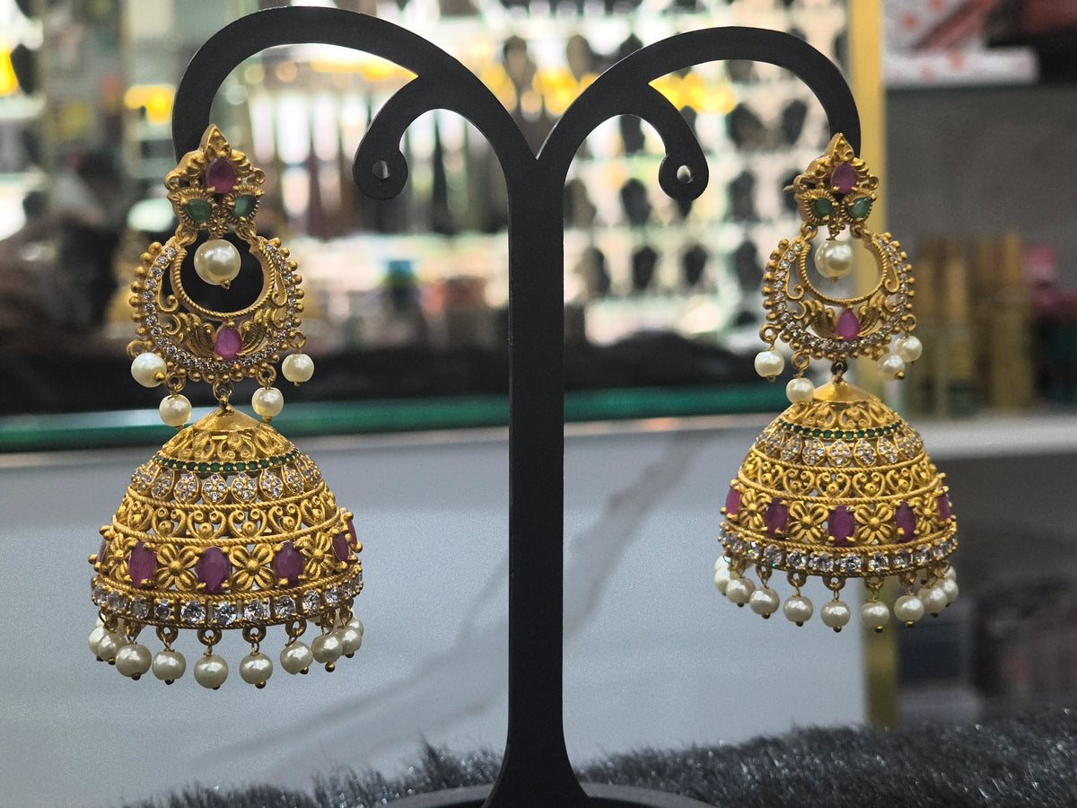 Ornate gold earrings with pearls and gemstones on a black stand.